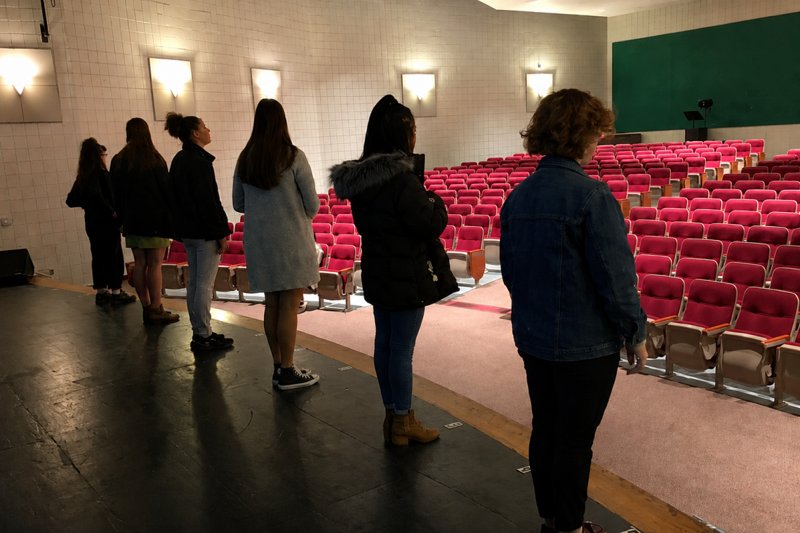 students standing on stage in an empty auditorium