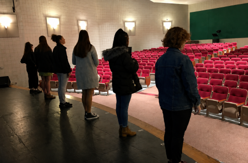 students standing on stage in an empty auditorium